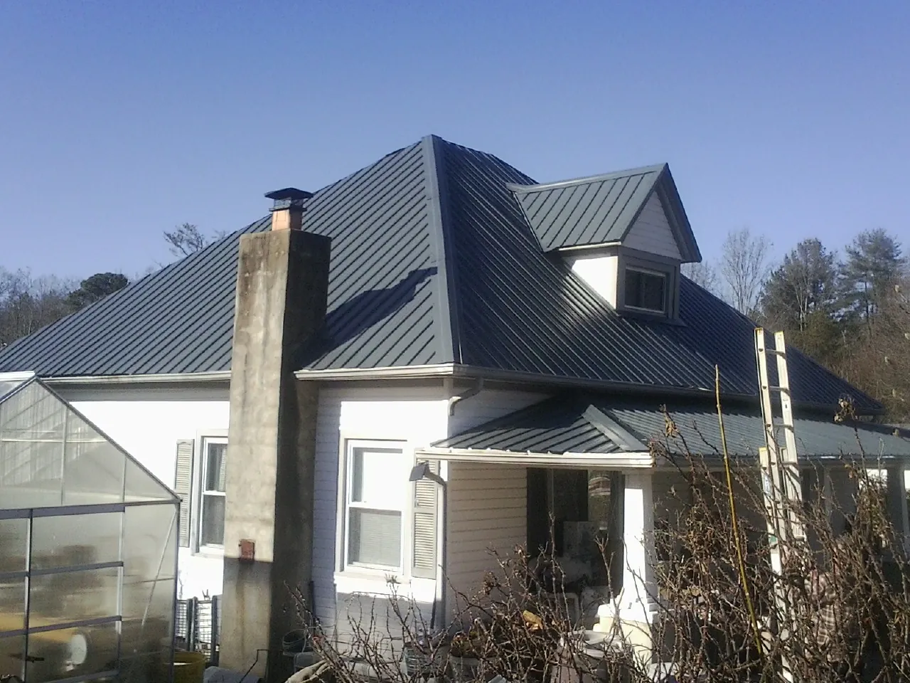 Dark blue standing seam metal roof on a white farmhouse with dormer — Slate & Tile Roof Repair by Roofing Brothers in Pflugerville