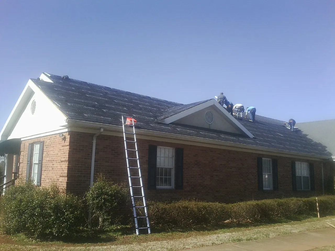 Crew tearing shingles off a brick ranch roof with a ladder set — Metal Roof Repair work by our crew in Pflugerville