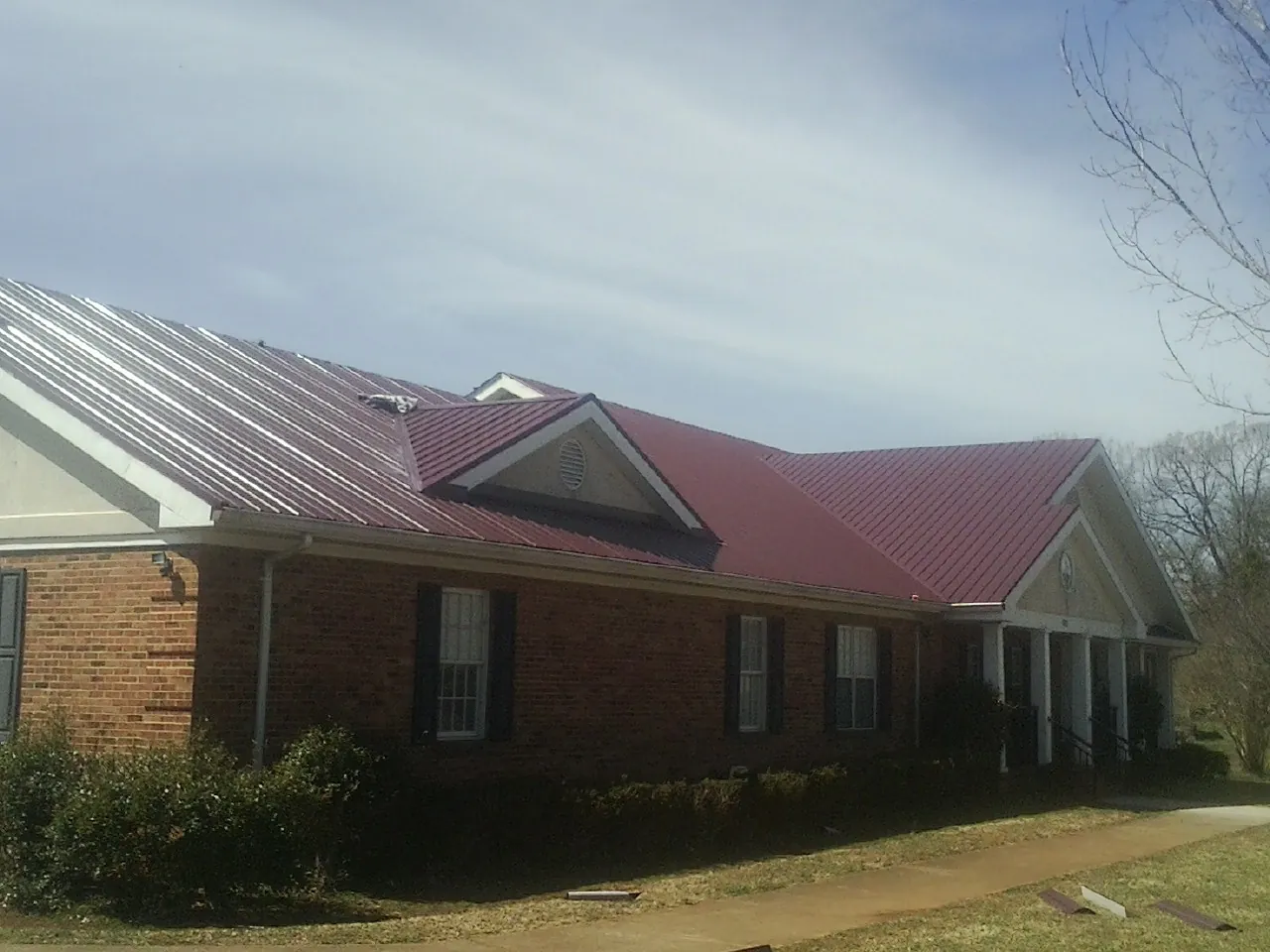 Red metal roof with gabled entries on a long brick building, from a Hail Damage Roof Repair job in Pflugerville