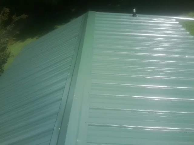 New green metal panels meeting at the ridge of a roof — Flat Roof Repair work by our crew in Pflugerville