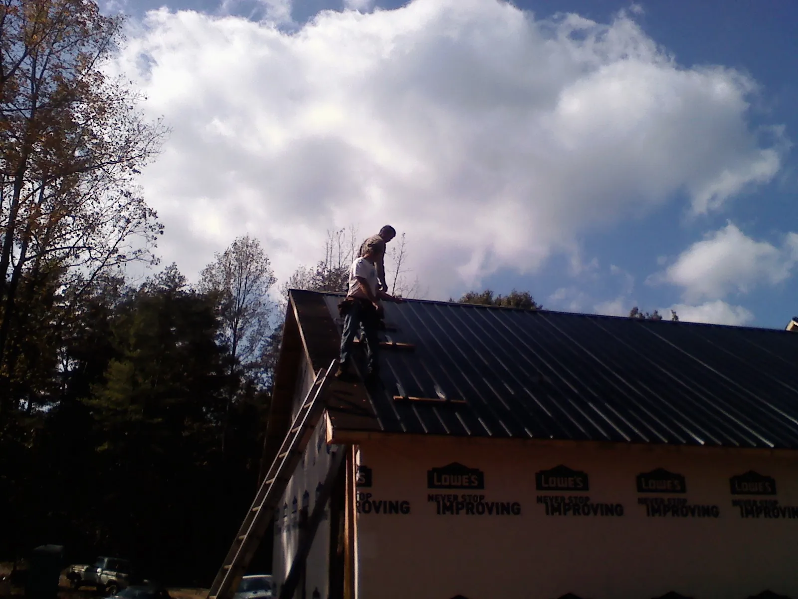 Roofer fastening dark metal panels high against a cloudy sky, from a Roof Inspection job in Pflugerville