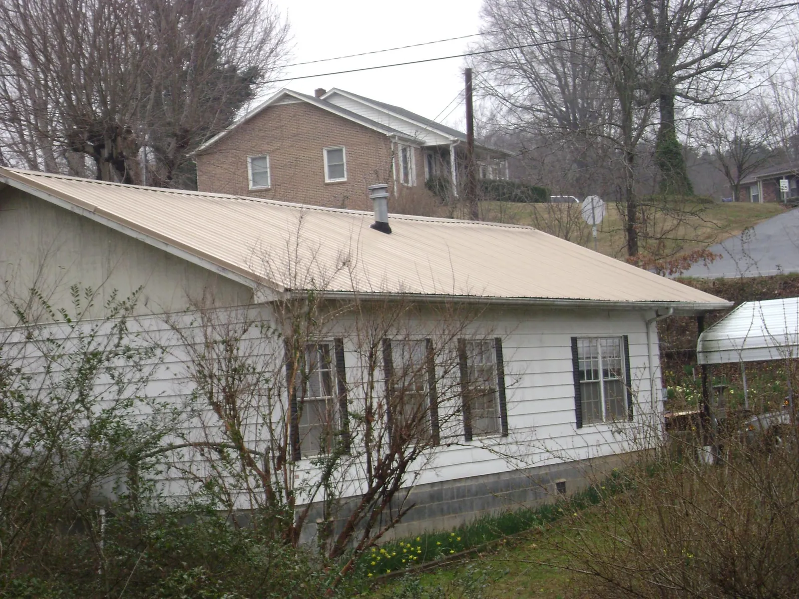 Tan metal roof on a white sided house set into a hillside — Commercial Roofing by Roofing Brothers in Pflugerville